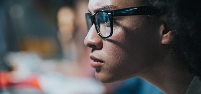 Pictorial representation of remote code execution in AI and machine learning libraries. Close-up of a woman wearing glasses and focusing intently on a computer screen.